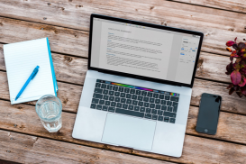 Laptop Computer with typing on screen and a notebook with pen